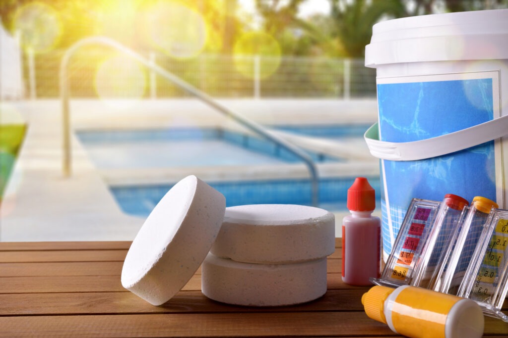 Swimming pool service and equipment with chemical cleaning products and tools on wood table and pool background